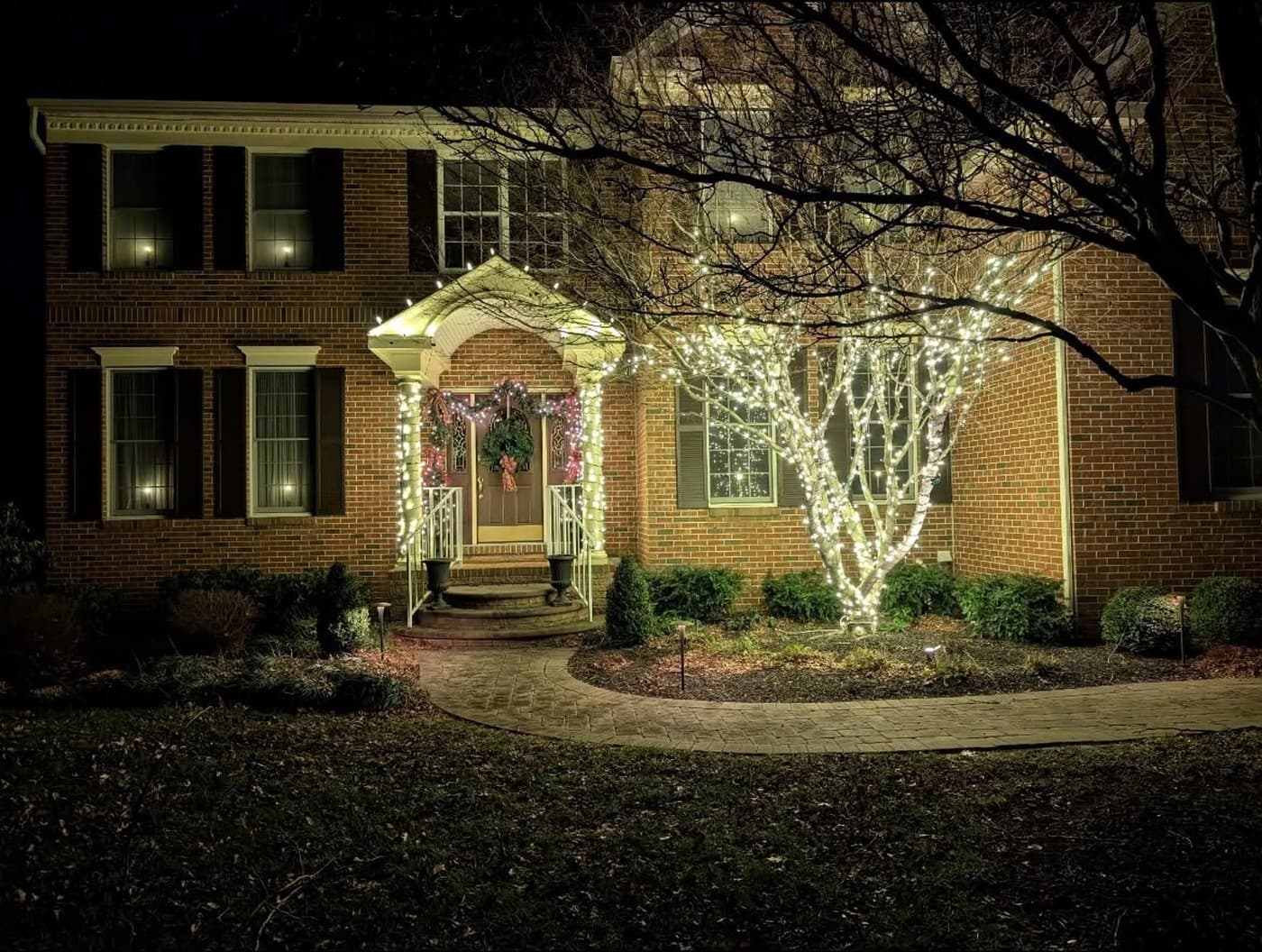 A brick home with warm white Christmas lights around the entrance and trees